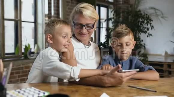 一幅可爱的祖母和她的孙子们坐在家里的桌子上用平板电脑进行视频聊天的画像视频的预览图