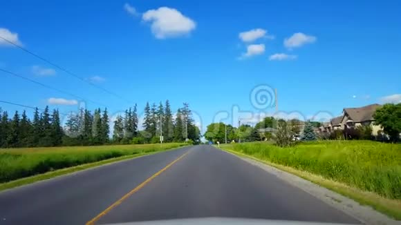 在明亮的夏日沿着乡村道路行驶司机视角POV美丽的郊区房屋视频的预览图