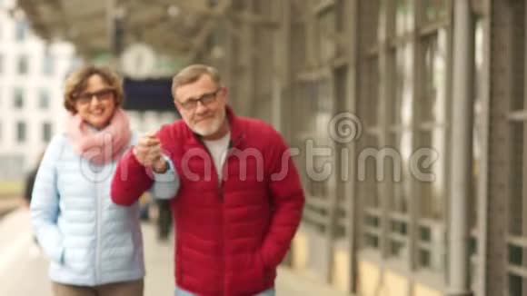一对可爱的成熟夫妇散步的肖像夫妻俩牵着手在城市里走来走去笑养恤金领取者视频的预览图