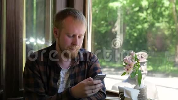 年轻的金发男人在咖啡馆里从一次性杯子里喝咖啡一个人手里拿着一部电话午休时间苏德视频的预览图
