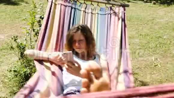 年轻女子在吊床上荡秋千在大自然中使用智能手机视频的预览图