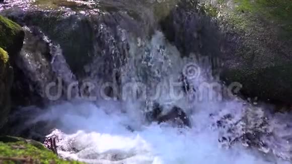 天然级联在覆盖着绿色苔藓的大石头之间使飞溅的淡水和纯净的水和泡沫进入视频的预览图