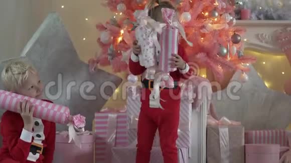 穿着圣诞老人服装的小男孩和小女孩拆掉他们的圣诞礼物视频的预览图