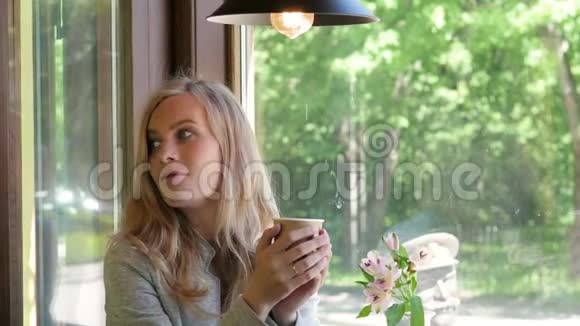 年轻的金发女人正在从纸杯里喝茶咖啡要走了在窗边的咖啡馆里吃早餐妇女视频的预览图