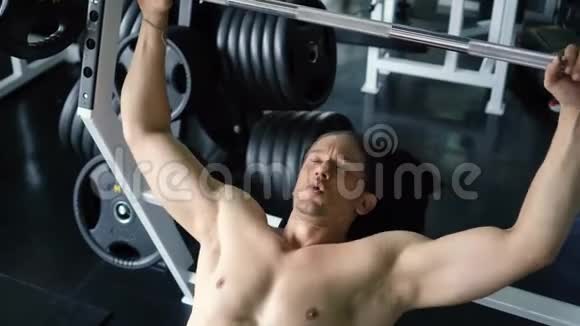 在健身房做杠铃式长凳按压运动的肌肉男视频的预览图