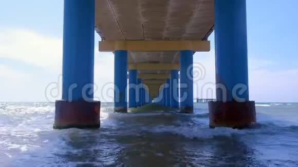 在平行的蓝色柱子之间的码头下的海在水中形成狭窄的走廊视频的预览图