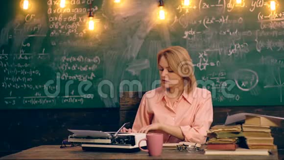 一位老师坐在学校的一个桌子旁用打字机打字桌上放着一块绿色的木板视频的预览图