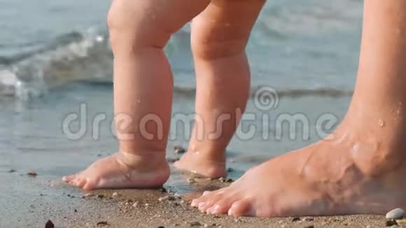 妈妈教宝宝在海滩散步孩子们的脚在沙滩上视频的预览图