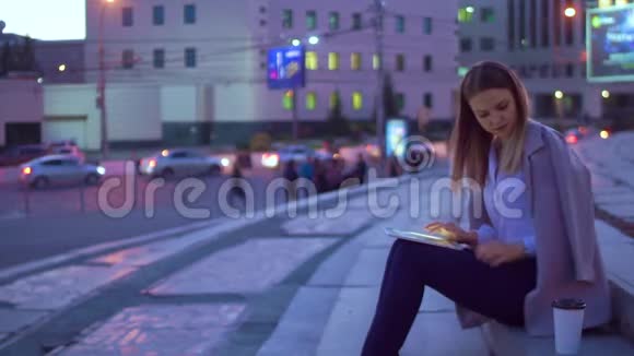 女孩在平板电脑里工作晚上在市中心喝咖啡视频的预览图