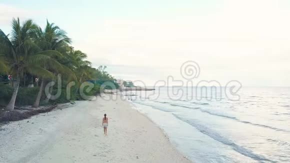 无人机观景女行走在海边的沙滩上空中风景女孩在天际线上的热带海滩视频的预览图