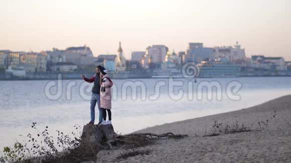 情侣在秋天的海滩上在河和城市的背景下自拍4K慢慢视频的预览图