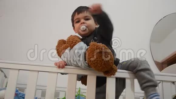 可爱的两岁小孩抱着穿着婴儿身服的玩具熊打电话给妈妈把他从床上抱下来视频的预览图