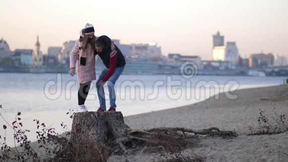 情人们男孩把女孩抱在怀里一对夫妇站在河边的树桩上视频的预览图