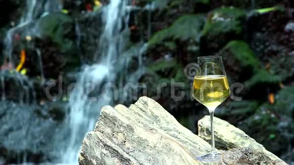 一杯白葡萄酒矗立在背景的木制表面上一块有瀑布的岩石视频的预览图