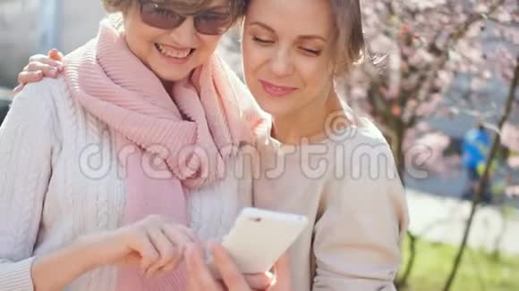 两个手里拿着智能手机的成年女人站在大街上站在春暖花开的背景下视频的预览图