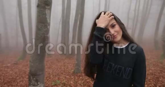 秋天的震动雾蒙蒙的森林漂亮的黑发女人长发穿着休闲装穿过森林视频的预览图