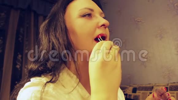 一位身着白袍的年轻女子用鲜艳的红色唇膏涂抹嘴唇视频的预览图