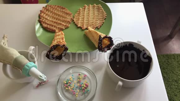 桌子上放着一个华夫饼锥蘸着融化的巧克力用多种颜色的花洒装饰有c的成分视频的预览图