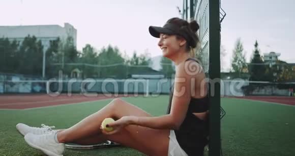 比赛结束后一位有魅力的年轻女子休息了一下坐在地板上玩网球微笑着视频的预览图