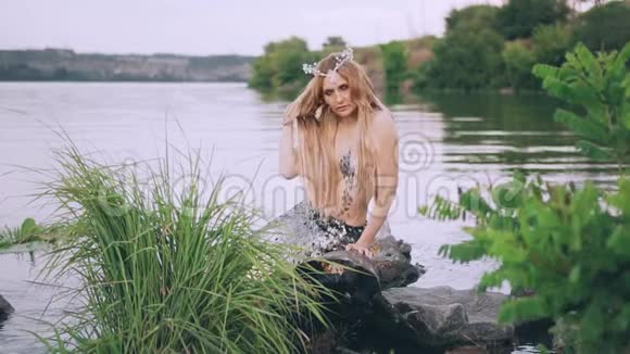 金发碧眼的少女头上戴着一顶美人鱼珍珠王冠头上戴着一条豪华的银色尾巴坐在靠近木头的地方视频的预览图