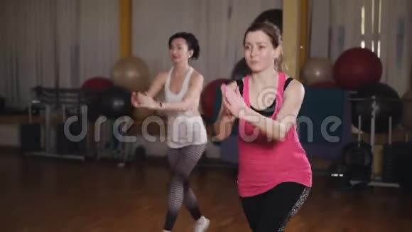 两个漂亮的运动女孩蹲在健身房里两个女孩在台上用哑铃做步健美操视频的预览图