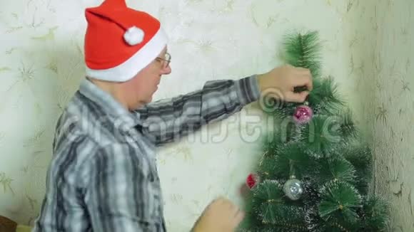 戴圣诞老人帽子的人在圣诞树上挂一个喜庆的球视频的预览图