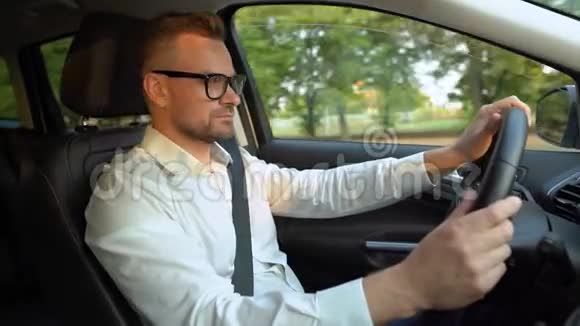 在阳光明媚的天气里戴着眼镜和白衬衫的胡子男人开着一辆车侧视图视频的预览图