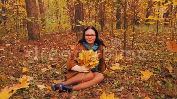 秋天公园的草地上一个戴着眼镜的年轻女子手里拿着枫叶视频的预览图