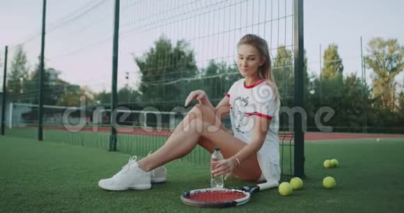 令人惊奇的是一个可爱的金发女孩打开了一瓶静水在网球场上慢慢地喝着视频的预览图