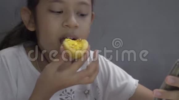 亚洲可爱的女孩吃甜食午餐时在餐馆里使用手机视频的预览图