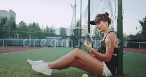 在网球场上一个零星的女人准备网球比赛坐在地板上放松视频的预览图