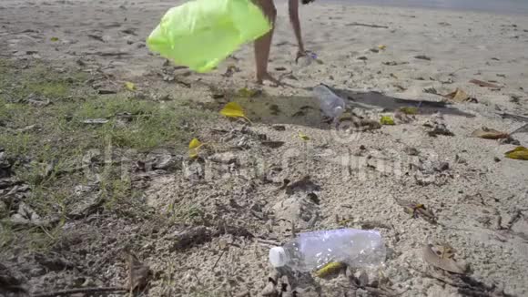 小女孩在沙滩上收集垃圾成绿色塑料袋塑料瓶在海滩上收集视频的预览图