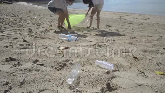 妈妈和女儿在沙滩上收集垃圾成绿色塑料袋塑料瓶在海滩上收集视频的预览图