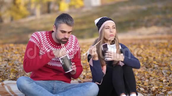 秋天海滩一个男人和一个女孩坐在毯子上吃着中国菜说话微笑视频的预览图