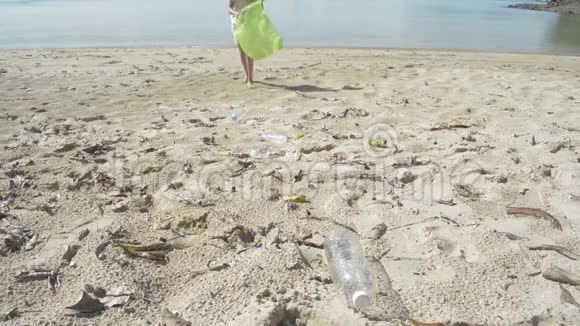 小女孩在沙滩上收集垃圾成绿色塑料袋塑料瓶在海滩上收集视频的预览图