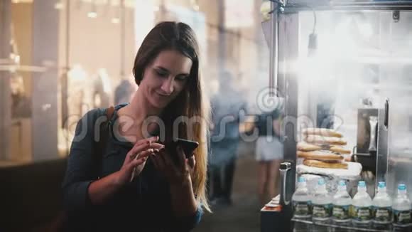 快乐美丽的白人女性博客使用智能手机购物应用程序附近的街道食品卡车与椒盐卷饼在纽约视频的预览图