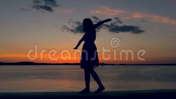 夕阳下的女人沿着海滨散步把手放在一边视频的预览图