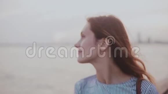 幸福体贴的年轻欧洲女孩的肖像头发随风飘扬夕阳河滩上平静的微笑视频的预览图
