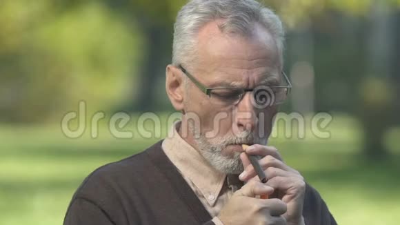 灰胡子男人坐在公园里吸雪茄烟享受味道和香气视频的预览图