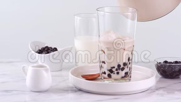 在玻璃杯中倒入奶茶在明亮的大理石桌面和白色托盘上泡上美味的台湾木薯珍珠泡自制自负视频的预览图