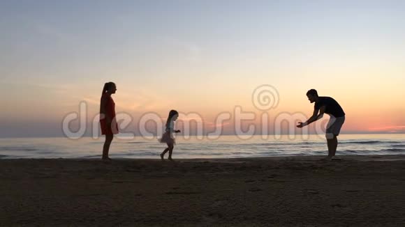 日落时小女孩沿着海滩在父母之间奔跑视频的预览图