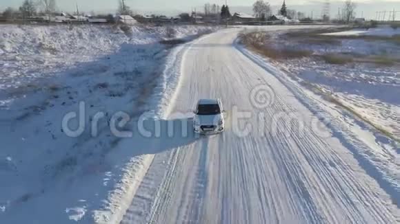 一辆孤独的白色汽车在俄罗斯一个小村庄的冬季道路上行驶的鸟瞰图库存录像美丽的霜冻视频的预览图