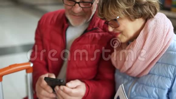 几位退休老人坐在机场的长凳上在等待他们的时候在智能手机上看照片视频的预览图