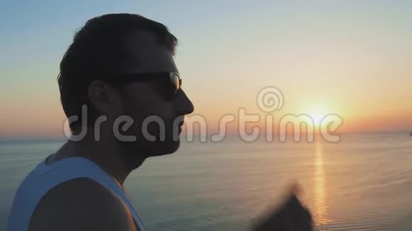 一个人沿着海岸跑在日落时做运动运动员听力音乐使用无线耳机的运动员视频的预览图