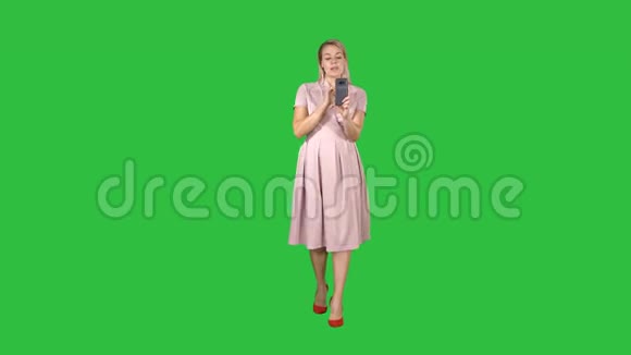微笑的女人穿着粉红色的衣服做视频电话走在绿色屏幕上Chroma键视频的预览图