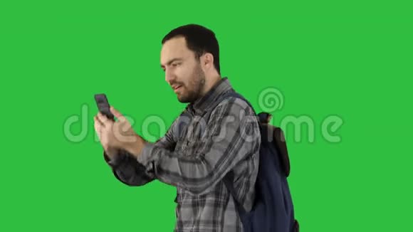 帅气的年轻人背着背包在绿色屏幕上给自己拍照彩色键视频的预览图
