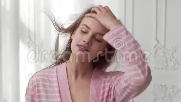 穿着浴衣的美女在充满阳光的卧室里用吹风机吹干头发护发快乐视频的预览图