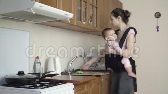 忙碌的母亲带着婴儿在家洗脏盘子视频的预览图