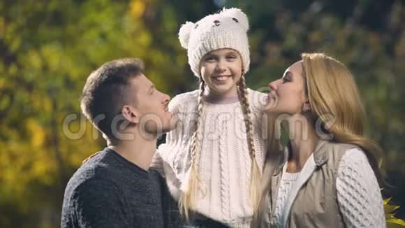 快乐的父母在秋园亲吻快乐的女儿富裕的家庭幸福的生活视频的预览图