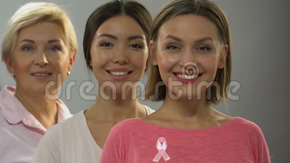 不同年龄的女性带着粉色丝带对着镜头微笑乳腺癌控制视频的预览图